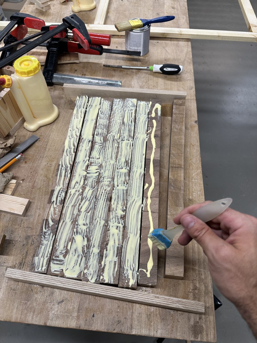 Woodworker spreading wood glue with a silicone brush across walnut strips